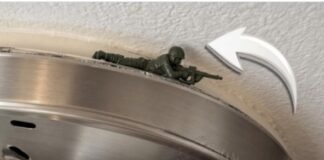 Imagem aproxima um pequeno soldadinho de plástico verde posicionado deitado, de barriga para baixo, sobre a borda metálica de uma luminária de teto, apontando sua arma para fora.