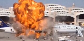 Ataques a aeroportos na Arábia Saudita deixam 12 mortos e mais de 300 feridos Grande explosão com chamas intensas e fumaça atingindo a lateral de um avião comercial de passageiros estacionado na pista de um aeroporto.