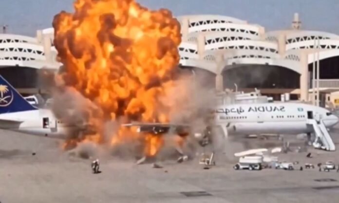 Grande explosão com chamas intensas e fumaça atingindo a lateral de um avião comercial de passageiros estacionado na pista de um aeroporto.