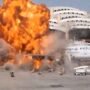 Ataques a aeroportos na Arábia Saudita deixam 12 mortos e mais de 300 feridos Grande explosão com chamas intensas e fumaça atingindo a lateral de um avião comercial de passageiros estacionado na pista de um aeroporto.