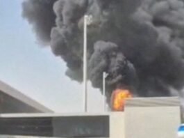 Após ataque fatal, houthis ameaçam espaço aéreo e paralisam voos na Arábia Saudita Densa nuvem de fumaça escura e chamas intensas subindo por trás do muro e da estrutura do terminal de um aeroporto, evidenciando uma forte explosão.