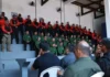 Primeira edição do curso de instrutores de armamento e tiro arranca em Rondônia Agentes de segurança pública perfilados numa bancada em formato de arquibancada, vestidos com fardas em tons de verde, vermelho e preto, durante a cerimónia de abertura da formação.