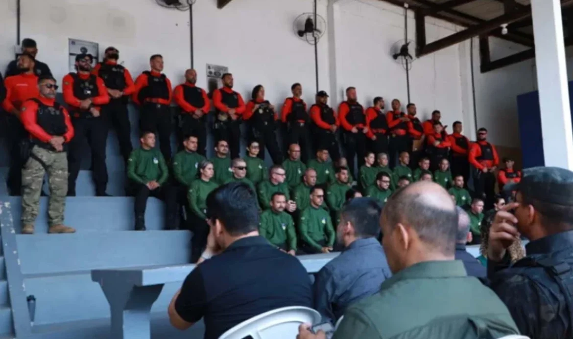 Agentes de segurança pública perfilados numa bancada em formato de arquibancada, vestidos com fardas em tons de verde, vermelho e preto, durante a cerimónia de abertura da formação.