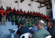 Agentes de segurança pública perfilados numa bancada em formato de arquibancada, vestidos com fardas em tons de verde, vermelho e preto, durante a cerimónia de abertura da formação.