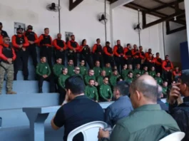 Primeira edição do curso de instrutores de armamento e tiro arranca em Rondônia Agentes de segurança pública perfilados numa bancada em formato de arquibancada, vestidos com fardas em tons de verde, vermelho e preto, durante a cerimónia de abertura da formação.
