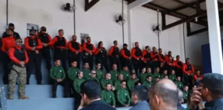 Agentes de segurança pública perfilados numa bancada em formato de arquibancada, vestidos com fardas em tons de verde, vermelho e preto, durante a cerimónia de abertura da formação.