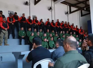 Primeira edição do curso de instrutores de armamento e tiro arranca em Rondônia Agentes de segurança pública perfilados numa bancada em formato de arquibancada, vestidos com fardas em tons de verde, vermelho e preto, durante a cerimónia de abertura da formação.