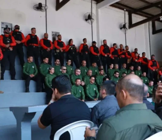 Primeira edição do curso de instrutores de armamento e tiro arranca em Rondônia Agentes de segurança pública perfilados numa bancada em formato de arquibancada, vestidos com fardas em tons de verde, vermelho e preto, durante a cerimónia de abertura da formação.
