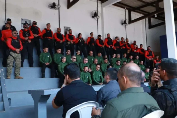 Agentes de segurança pública perfilados numa bancada em formato de arquibancada, vestidos com fardas em tons de verde, vermelho e preto, durante a cerimónia de abertura da formação.