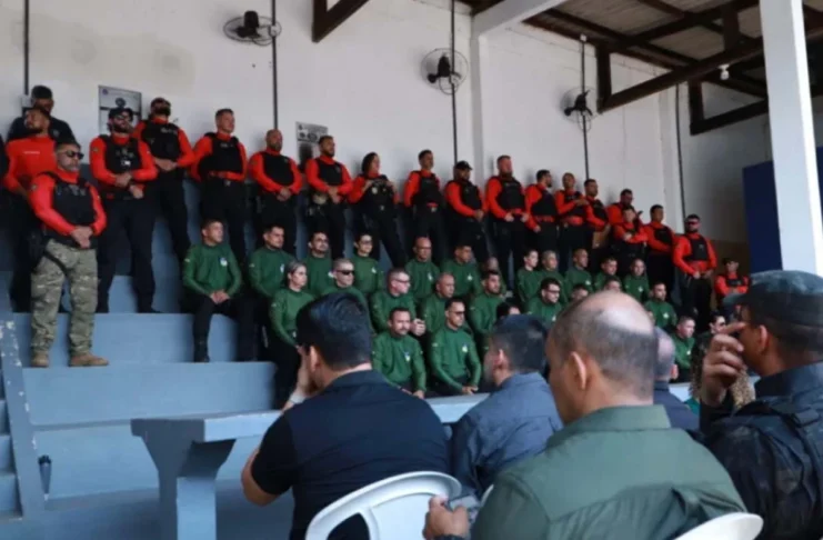 Agentes de segurança pública perfilados numa bancada em formato de arquibancada, vestidos com fardas em tons de verde, vermelho e preto, durante a cerimónia de abertura da formação.