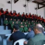Agentes de segurança pública perfilados numa bancada em formato de arquibancada, vestidos com fardas em tons de verde, vermelho e preto, durante a cerimónia de abertura da formação.