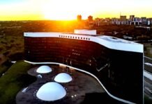 Vista aérea do edifício do Tribunal Superior Eleitoral (TSE) em Brasília, exibindo a sua arquitetura com fachada em curva negra e branca sob a luz de um pôr do sol.