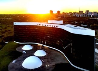Vista aérea do edifício do Tribunal Superior Eleitoral (TSE) em Brasília, exibindo a sua arquitetura com fachada em curva negra e branca sob a luz de um pôr do sol.