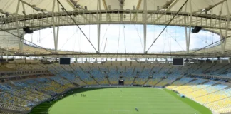 Vista panorâmica interna do estádio do Maracanã, com o gramado verde em destaque e as arquibancadas vazias, sob o teto coberto da arena.