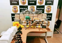 Mesa exibindo diversos pacotes de drogas empilhados, ladeados por seis revólveres, pistolas, um fuzil e dezenas de munições, com um painel da Polícia Civil ao fundo.