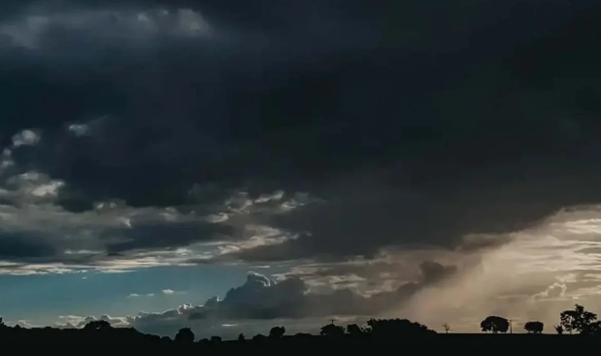 Céu escuro coberto por nuvens pesadas de tempestade sobre uma paisagem rural com silhuetas de árvores no horizonte.