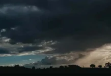 Céu escuro coberto por nuvens pesadas de tempestade sobre uma paisagem rural com silhuetas de árvores no horizonte.