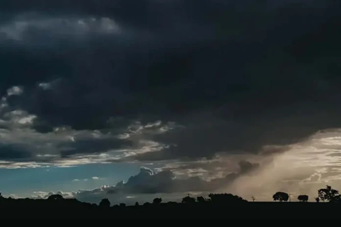 Nuvens carregadas anunciam chuva forte no Norte Céu escuro coberto por nuvens pesadas de tempestade sobre uma paisagem rural com silhuetas de árvores no horizonte.