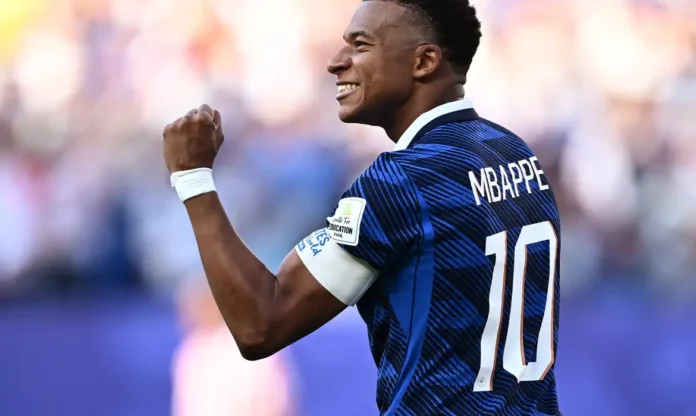 O jogador Mbappé sorrindo e comemorando em campo, vestindo a camisa azul da seleção francesa de futebol.
