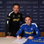 O jogador Cole Palmer assina um contrato sentado à mesa, com uma camisa do Chelsea ao lado, enquanto o técnico Xabi Alonso posa em pé, logo atrás dele.