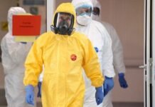 Ilustração laboratorial ou imagem de profissional de saúde com vestimenta de proteção examinando amostras biológicas em área de contenção epidemiológica.