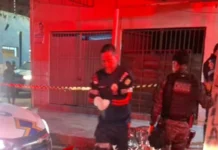 Homem é assassinado a tiros por dupla de moto perto do Mercado do Peixe Profissional do Samu de luvas brancas e policial militar do batalhão de Choque trabalhando em uma cena de crime à noite, com área isolada por fita zebrada.