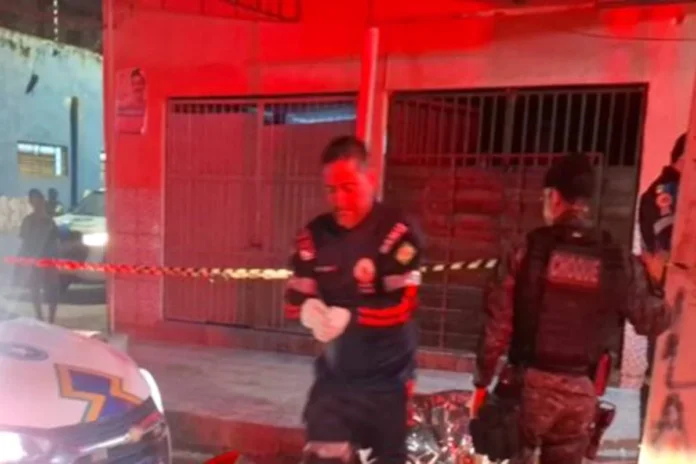 Profissional do Samu de luvas brancas e policial militar do batalhão de Choque trabalhando em uma cena de crime à noite, com área isolada por fita zebrada.