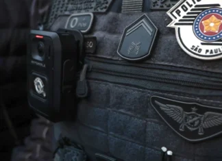 Três suspeitos morrem em tiroteio com a Polícia Militar durante assalto em São Paulo Colete tático escuro de um agente da Polícia Militar de São Paulo, equipado com uma câmara corporal (bodycam) e ostentando as insígnias oficiais da corporação.