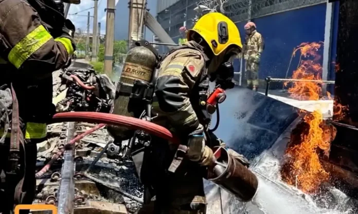 Bombeiros combatem chamas em destroços de avião em BH Bombeiro militar, utilizando capacete amarelo e equipamento de proteção respiratória, combate as chamas com uma mangueira de água sobre os destroços de uma aeronave acidentada.