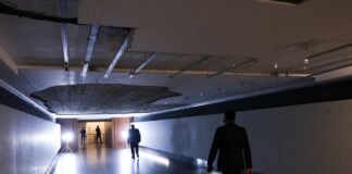Corredor do Túnel do Tempo na Câmara dos Deputados com um buraco visível no teto devido à queda do reboco, iluminado por holofotes e com a silhueta de homens a caminhar.