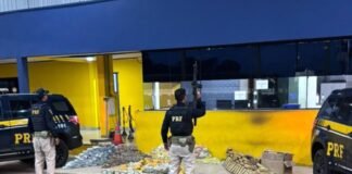 PRF apreende quase 500 quilos de droga em veículo de carga na BR-364 em Pimenta Bueno Agentes da Polícia Rodoviária Federal armados em frente ao posto policial, junto a duas viaturas pretas e dezenas de pacotes de droga apreendidos dispostos no chão.