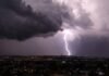 Trovoadas ganham força e atingem Rondônia e mais quatro estados do Norte Céu noturno coberto por nuvens escuras de tempestade sobre uma cidade, com um raio forte caindo e iluminando o horizonte.