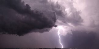 Céu noturno coberto por nuvens escuras de tempestade sobre uma cidade, com um raio forte caindo e iluminando o horizonte.