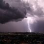 Trovoadas ganham força e atingem Rondônia e mais quatro estados do Norte Céu noturno coberto por nuvens escuras de tempestade sobre uma cidade, com um raio forte caindo e iluminando o horizonte.