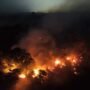 Amazonas registra aumento de 271% nos focos de incêndio em outubro; fumaça afeta saúde da população Vista aérea noturna de uma extensa área de floresta em chamas, com grandes focos de fogo alaranjado e muita fumaça subindo pelo escuro.